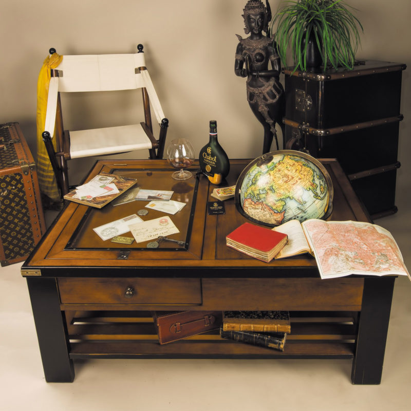 Interior wuth Unique coffee table featuring globe and glass panel to display ephemera. Coffee table has brass hardware, one large drawer, book and magazine rack below. Table has distressed French honey finish with black accents