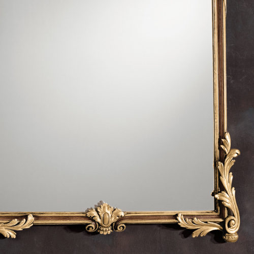 This carved wood framed vertical mirror is hand crafted in Louis XV style. Wall mirror has intricately carved frame richly embellished with scrolled leaf corners, a small elegant cartouche on the bottom center, and graceful leaf swags with rising leaf on the top. Louis XV mirror has a hand painted medium brown finish and antiqued gold leaf accents. This mirror is hand-crafted in Italy