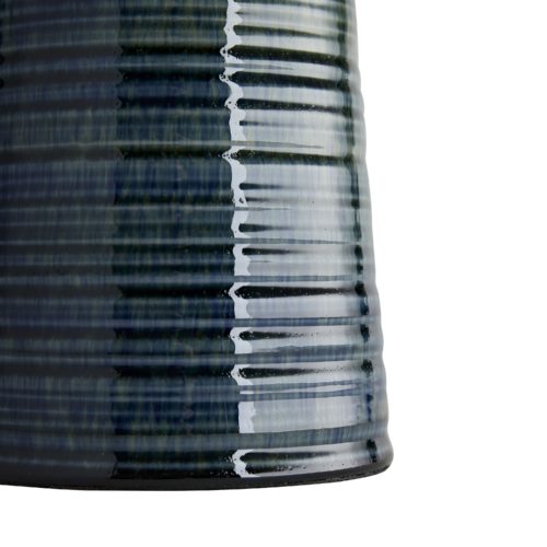 Starting from the tiered disk-shaped neck, a bronze and peacock reactive glaze breaks over the porcelain foundation to create a devastatingly beautiful aesthetic. The handcrafted elements of this pieceare evident, especially in the ribbed details that catch the finish and pull heavier in its grooves.