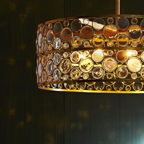 Transform a space with this luxe luminescent. Eight arms extend from an antique brass steel pipe, gracefully suspending a clear crystal shade that has been adorned with brass rings. Each ring that scapes the façade has been skillfully applied byhand. The semi-open form of the shade maximizes the design of the circular pattern.
